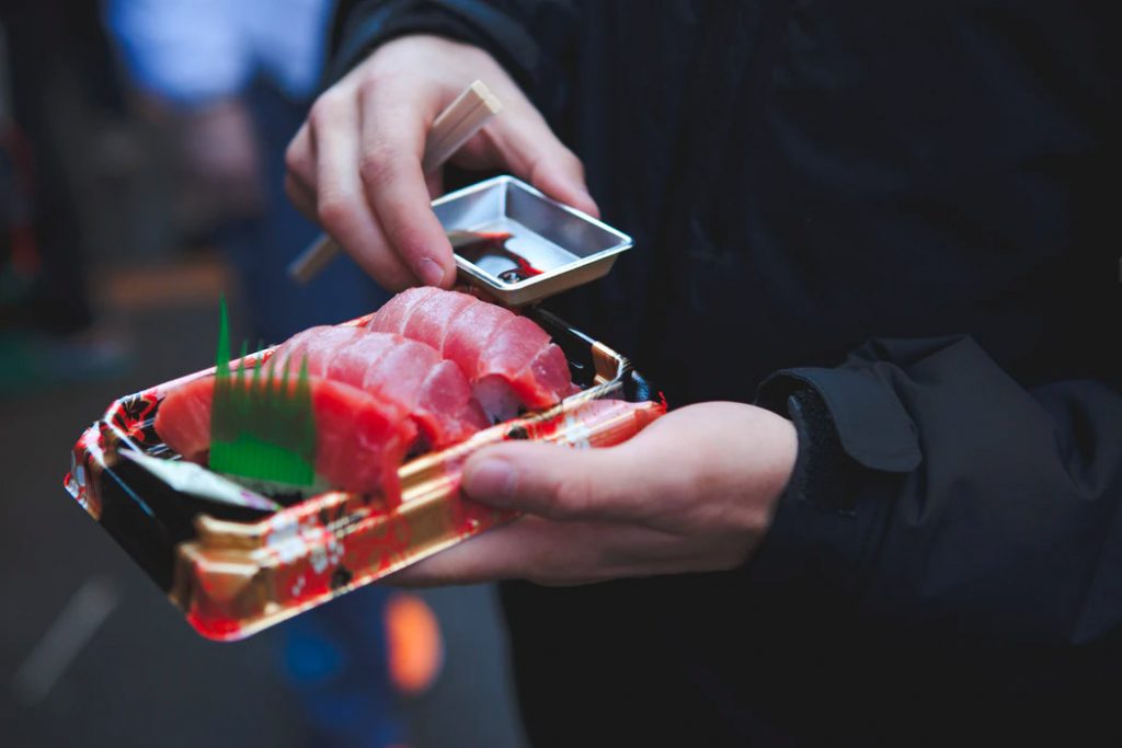 A man carrying sushi with soy sauce and chopsticks
