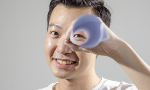 A man holds a rolled up piece of paper to his eye