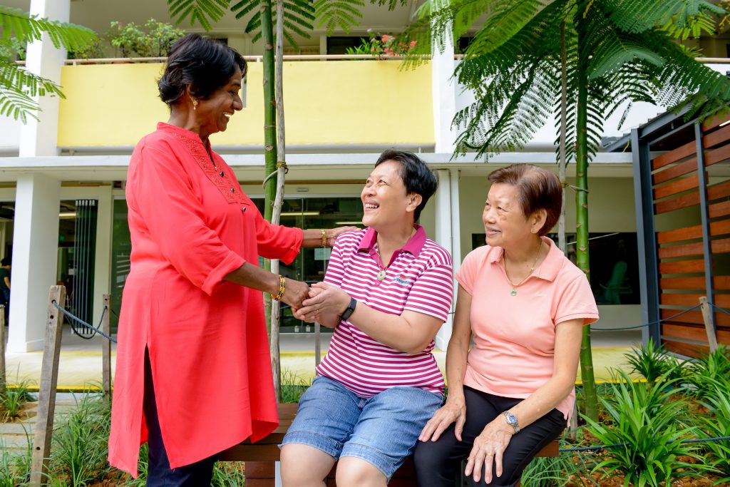 A group of middle-aged to elderly ladies, some are seated and one is standing, happily chatting.